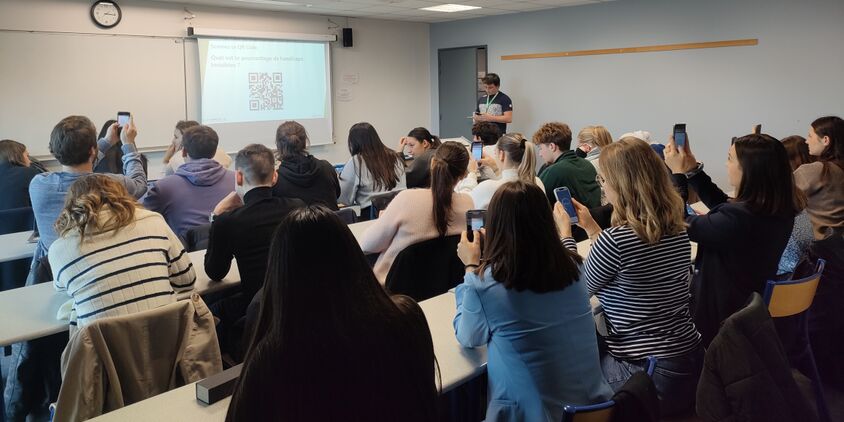 Etudiants dans une salle de classe scannent le QR CODE affiché au tableau pour répondre à un quiz sur le handicap.
